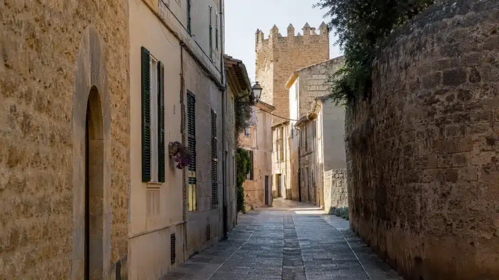 Historische Gasse in der Altstadt von Alcúdia mit Natursteinmauern und mittelalterlichem Turm