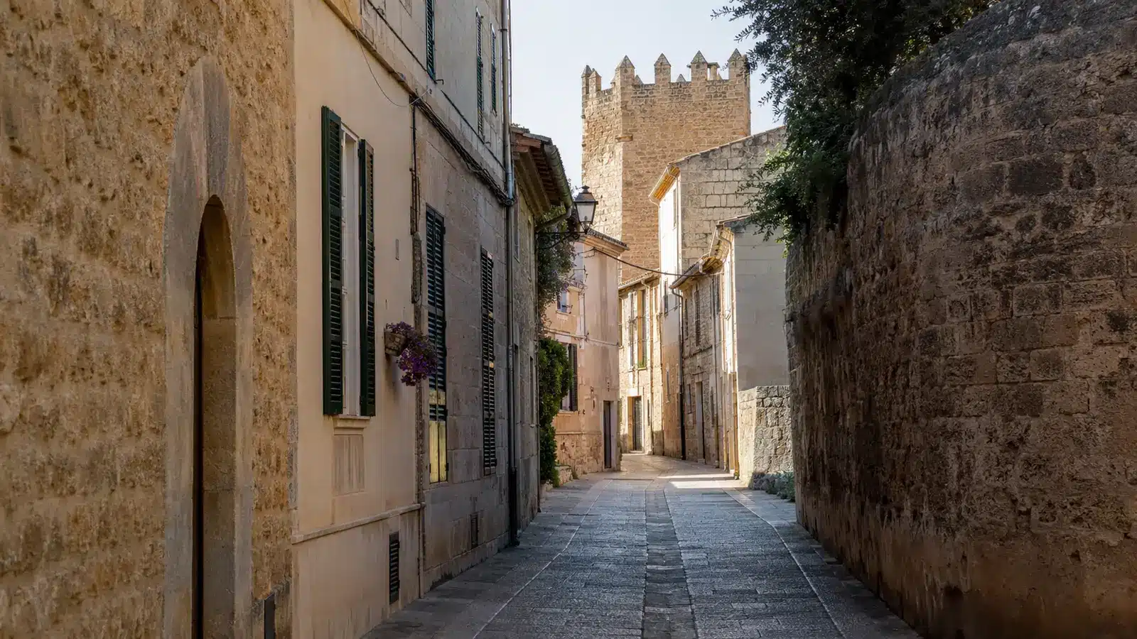 Historische Gasse in der Altstadt von Alcúdia mit Natursteinmauern und mittelalterlichem Turm
